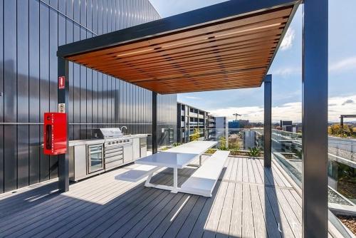 una terraza de madera con mesa y una cocina en un edificio en Mulberry 2BR-2BA Rooftop Pool, BBQ, WiFi & Netflix - Central Location en Canberra