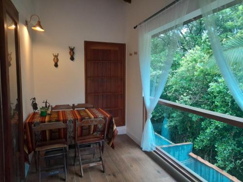a dining room with a table and a large window at Hakuna Studios Barra do Sahy in Barra do Sahy