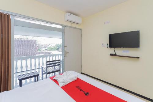 a room with a bed and a tv and a balcony at RedDoorz at CBR Residence Blimbing in Malang