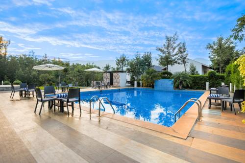 a swimming pool with tables and chairs and an umbrella at The Blossom Resort - Chikmagalur in Chikmagalūr