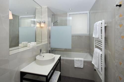 a white bathroom with a sink and a bath tub at Hôtel Tourisme Avenue in Paris