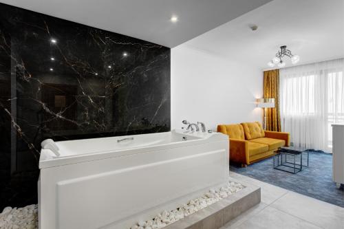 a bathroom with a white tub and a yellow couch at Hotel Pegaz in Krynica Zdrój