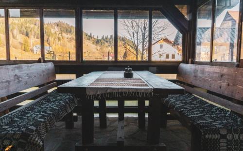 einen Tisch und Bänke in einem Zimmer mit Fenstern in der Unterkunft Casa Cristina in Fundu Moldovei