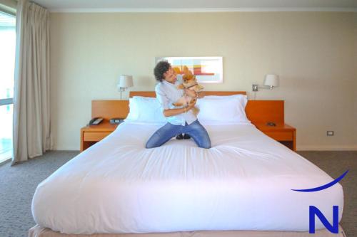 a man sitting on a bed holding a dog at Novotel Puerto Montt in Puerto Montt