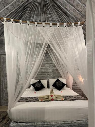 1 cama con dosel y cortinas y almohadas blancas en The Ocean Sunset Villas Ceningan, en Nusa Lembongan