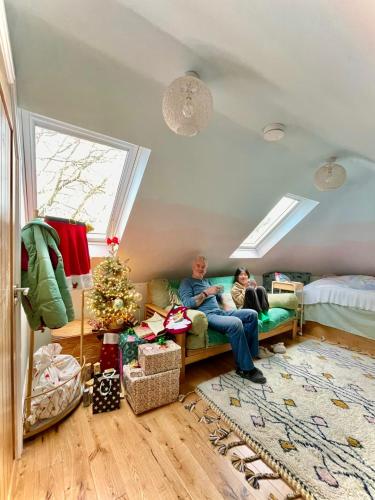 two people sitting on a couch in a room with a christmas tree at The Millers Cottage in Cambridge