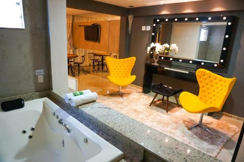 a bathroom with a tub and two yellow chairs at Hotel Pedra Negra Gov. Valadares in Governador Valadares