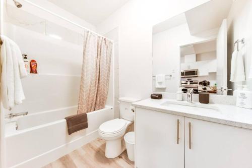 een witte badkamer met een toilet, een bad en een wastafel bij Cozy Nordic Utopia, Bsmt Suite near WEM & DT, King Bed, WiFi in Edmonton