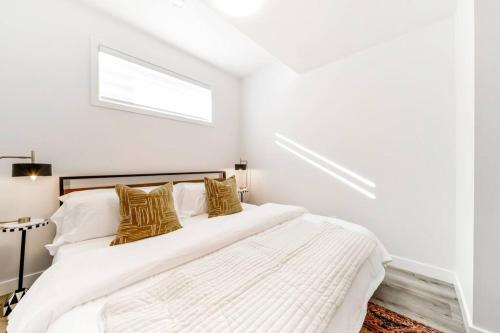 a white bedroom with a large bed with gold pillows at Cozy Nordic Utopia, Bsmt Suite near WEM & DT, King Bed, WiFi in Edmonton