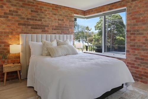 a bedroom with a white bed and a brick wall at Pelican Waters in Merimbula