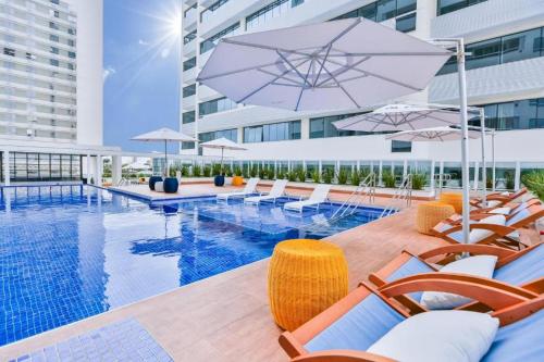 uma piscina com cadeiras e guarda-sóis ao lado de um edifício em Apart-hotel América B em Campos dos Goytacazes