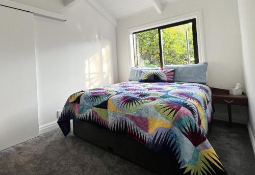 una camera da letto con un letto con un piumone colorato e una finestra di The Partchery Devonport ad Auckland