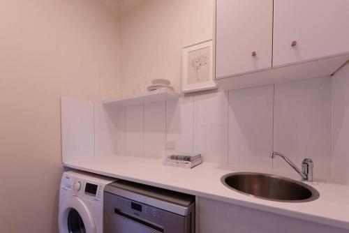 una cucina bianca con lavandino e lavatrice di Campbells Cottage by Ready Set Host a Frankston