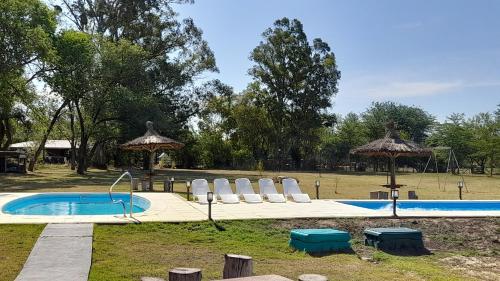 una piscina con sillas y sombrillas en un parque en Cabañas La Deseada (Ranchos, Buenos Aires) en Ranchos