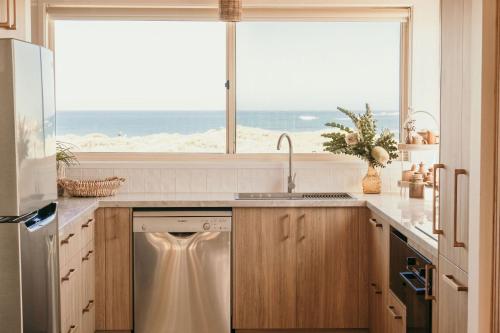 a kitchen with a dishwasher and a window with the ocean at Sunsets on Martyrs Luxury Coastal Beach House Peterborough in Peterborough