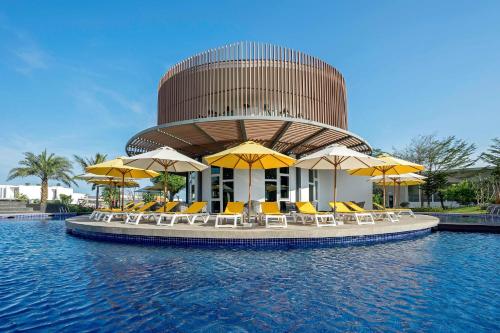 un edificio circular con sillas y sombrillas en el agua en Oceanami villa Resort từ 1PN đến 5PN - Đầy đủ tiện nghi - Bếp nấu - BBQ - Hồ bơi - Sát Biển Long Hải - Hồ Tràm - Vũng Tàu, en Long Hai
