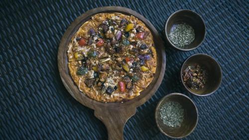 a pizza on a wooden plate on a table with spices at Bougainvillea Retreat & Spa in Kāhārpāra