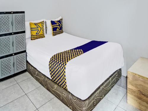 1 cama con sábanas blancas y almohadas amarillas y azules en OYO 92086 Fun Guesthouse Syariah, en Mojokerto
