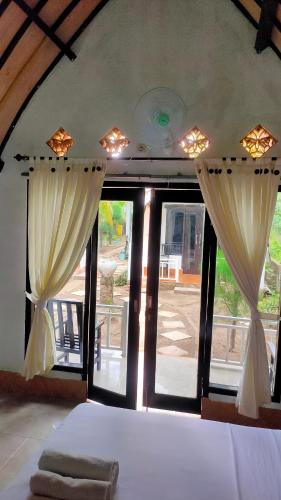 a bedroom with a bed and windows with curtains at Meno Lodge in Gili Meno