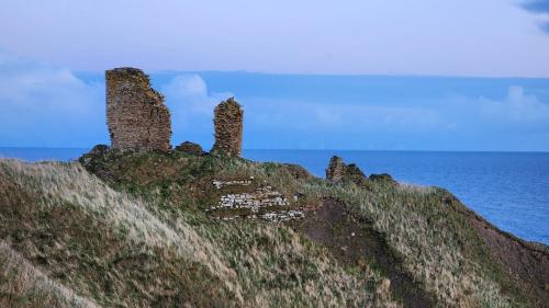 an old castle on top of a hill with the ocean at Castle Shieling in Latheron