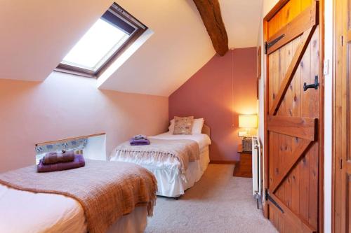 a attic bedroom with two beds and a window at Rustic Retreats: Owslow Cottage with hot tub & Alpaca Walking Experiences in Carsington