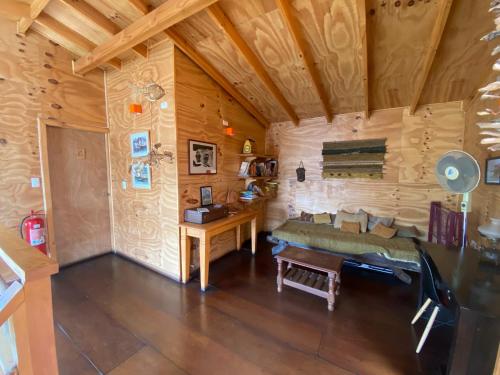 Habitación con sofá y escritorio en una cabaña de madera. en Hostal Palafito Waiwen en Castro