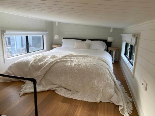 a bedroom with a bed with a white comforter and two windows at Tiny House Clunes at The Old Butter Factory in Clunes