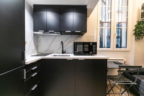 une cuisine avec des armoires noires et un four micro-ondes dans l'établissement Le studio de belleville 2 à 4 personnes, à Paris