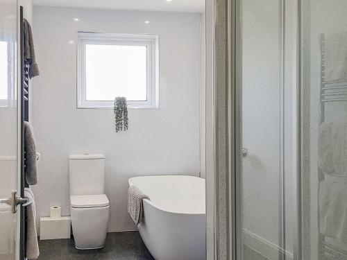 een badkamer met een bad, een toilet en een raam bij West Cottage in Fife