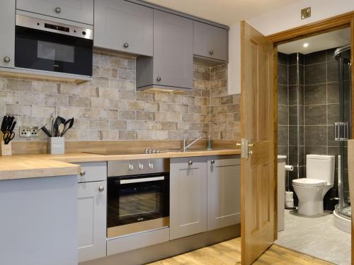 a kitchen with white cabinets and a sink and a toilet at The Byres Methera in St Bees
