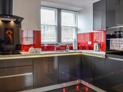 a kitchen with red and silver cabinets and a sink at Carse View Cottage in Abernethy