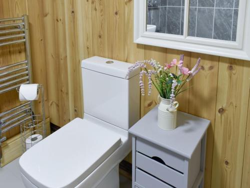 a bathroom with a white toilet and a vase of flowers at The Cabin in Elmstone