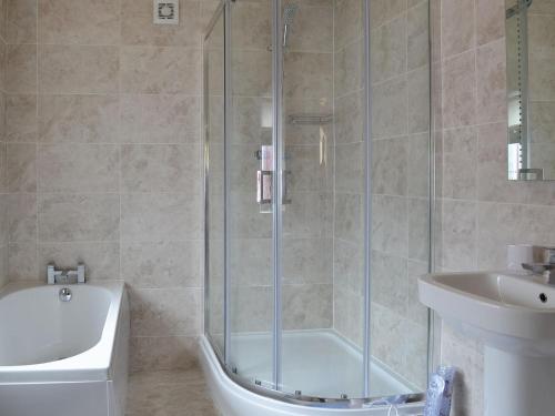 a bathroom with a shower and a tub and a sink at Puffin Cottage in Bempton