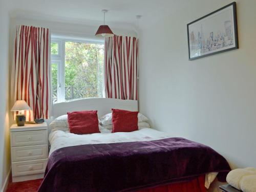 a bedroom with a bed with red pillows and a window at Tigh Beag in Troon