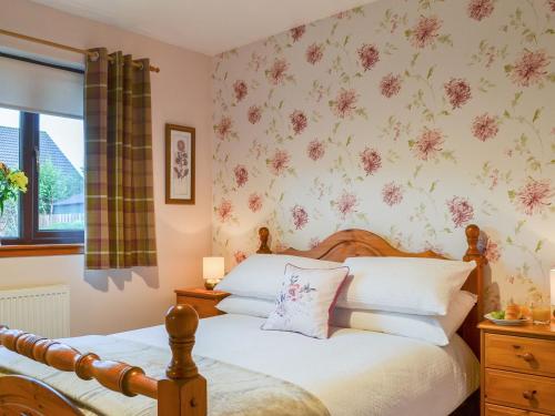 1 dormitorio con 1 cama con flores en la pared en Four Winds, en Drumnadrochit