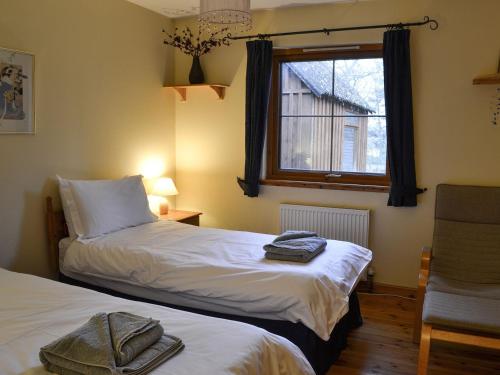 2 camas en una habitación con ventana y silla en Woodland Lodge, en Boat of Garten