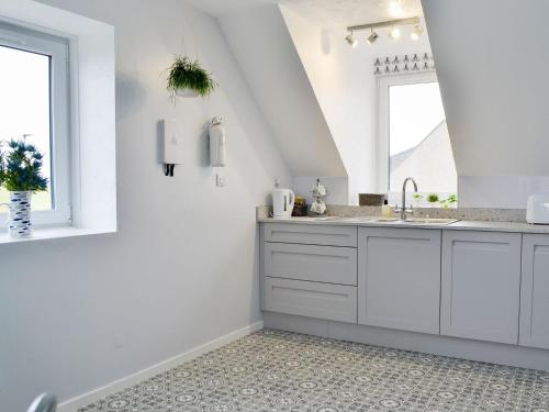 a white kitchen with a sink and two windows at Forvie View in Collieston