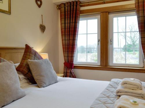 a bedroom with a bed with two windows at Baldowrie Farm Cottage in Ardler