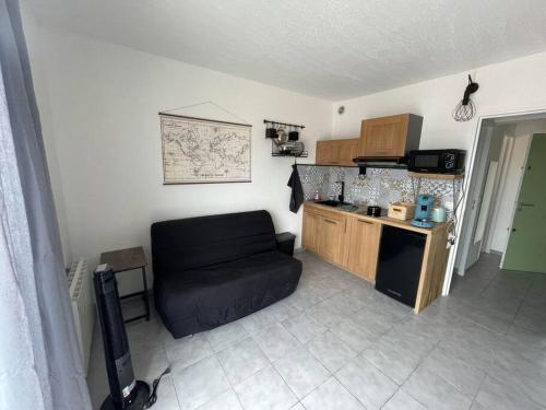 un salon avec un canapé noir et une cuisine dans l'établissement studio de la plage, à Saint-Cyprien
