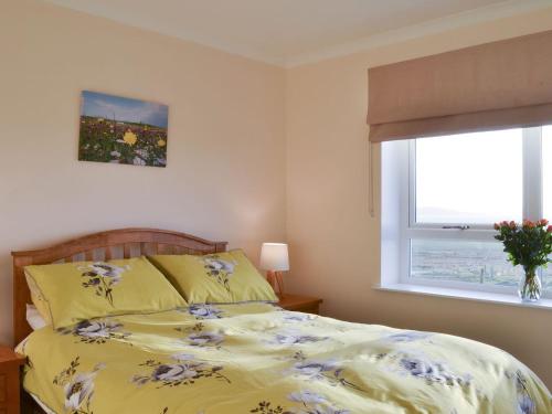 a bedroom with a bed with a yellow comforter and a window at West Kilbride in Pollachar