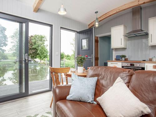 a living room with a leather couch and a kitchen at Moor Hen Shepherd Hut - Uk33888 in Cullompton