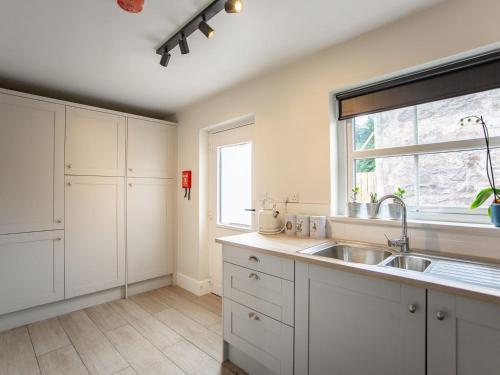 cocina con armarios blancos, fregadero y ventana en Flossys House -uk35020, en Chatton