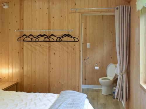 a bedroom with a bed and a toilet and wooden walls at Shepherds Hut 2 At Laddingford - Uk32534 in Yalding