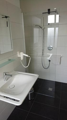 La salle de bains blanche est pourvue d'une douche et d'un lavabo. dans l'établissement Haus Fischer, à Norderney