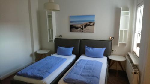 2 bedden in een kleine kamer met blauwe kussens bij Haus Fischer in Norderney