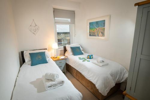 two twin beds in a room with a window at Woodland Cottage - cosy dog friendly cottage in the heart of Windermere in Windermere
