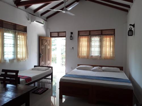 a bedroom with two beds and a table and windows at The Bamboo Leaf Apartment in Hikkaduwa