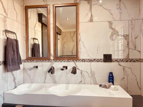 ein Badezimmer mit einem weißen Waschbecken und einem Spiegel in der Unterkunft Mndazi Manor in Pimville