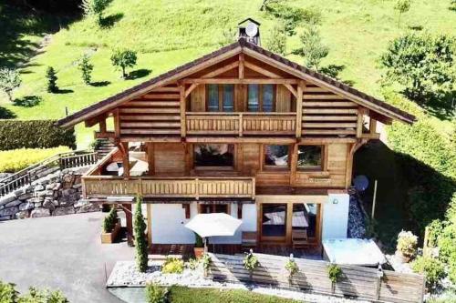 uma grande casa de madeira com uma colina verde em Androsace Appartement dans Chalet bois avec Jacuzzi privatif Terrasse et Vue Montagne em Les Villards-sur-Thônes
