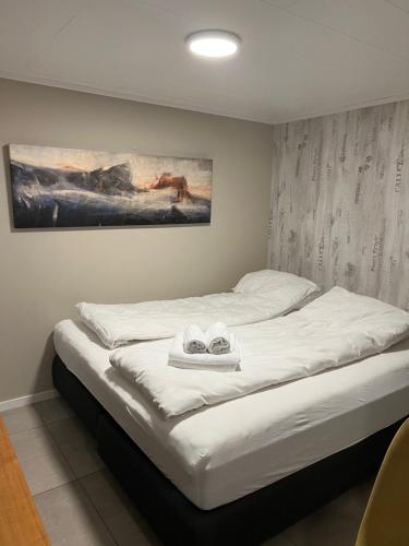 Håkøyveien 151, Tromsø في ترومسو: سرير بملاءات بيضاء ولوحة على الحائط